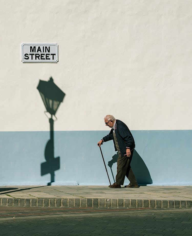 An Elderly Man Walking On The Sidewalk