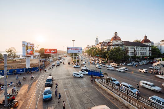 A vibrant urban intersection in Yangon, Myanmar, at sunset with vehicles and pedestrians.