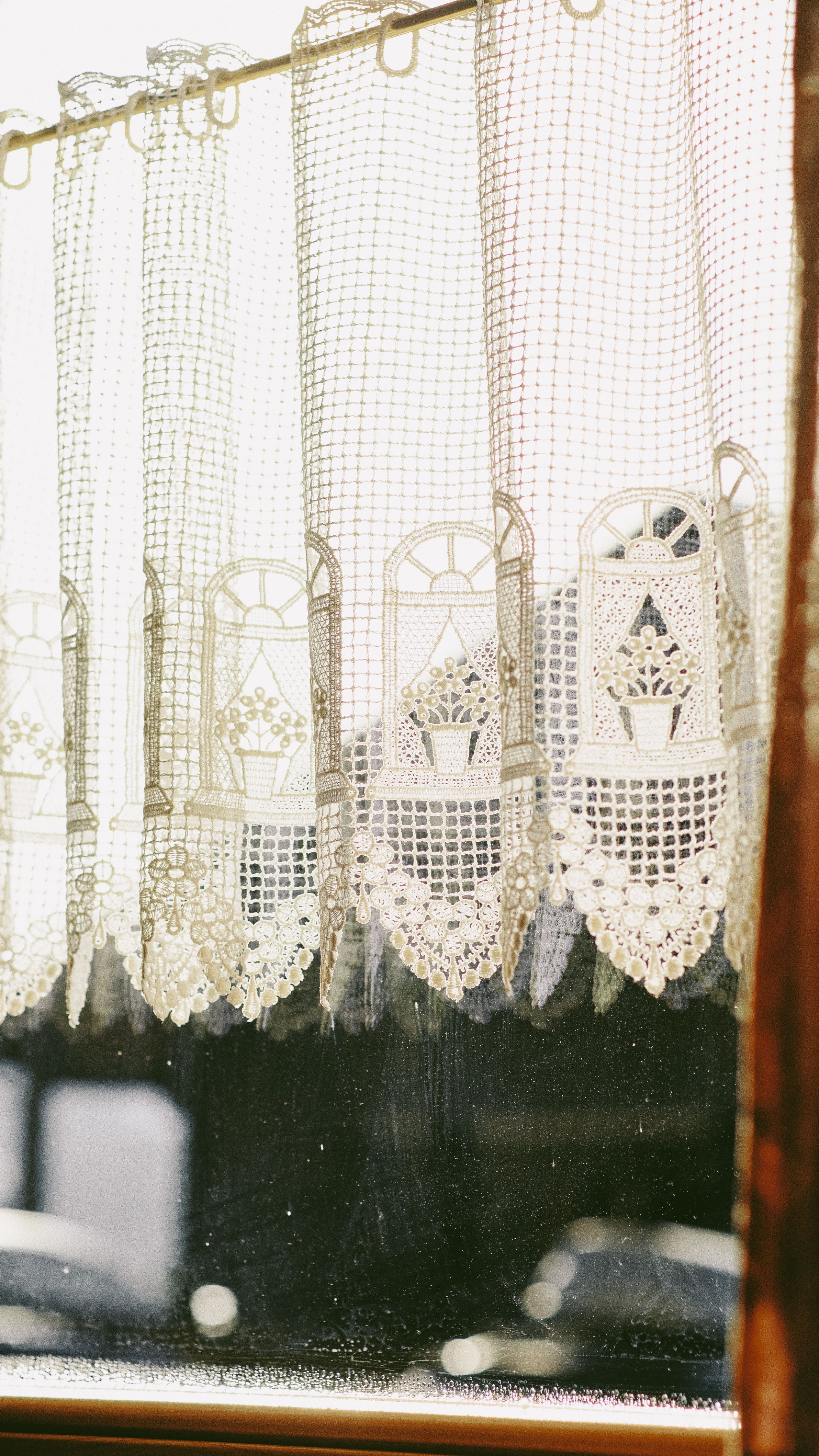 Delicate lace curtain hanging in a sunlit window with a vintage aesthetic.