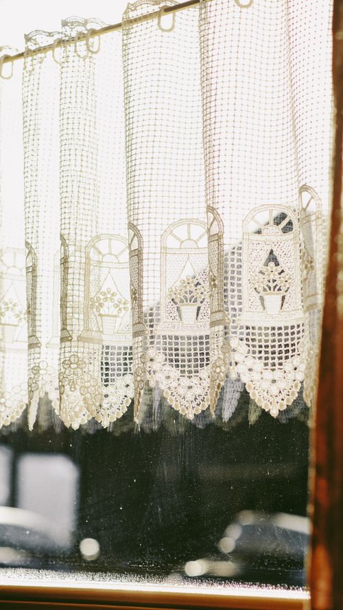 Free Delicate lace curtain hanging in a sunlit window with a vintage aesthetic. Stock Photo