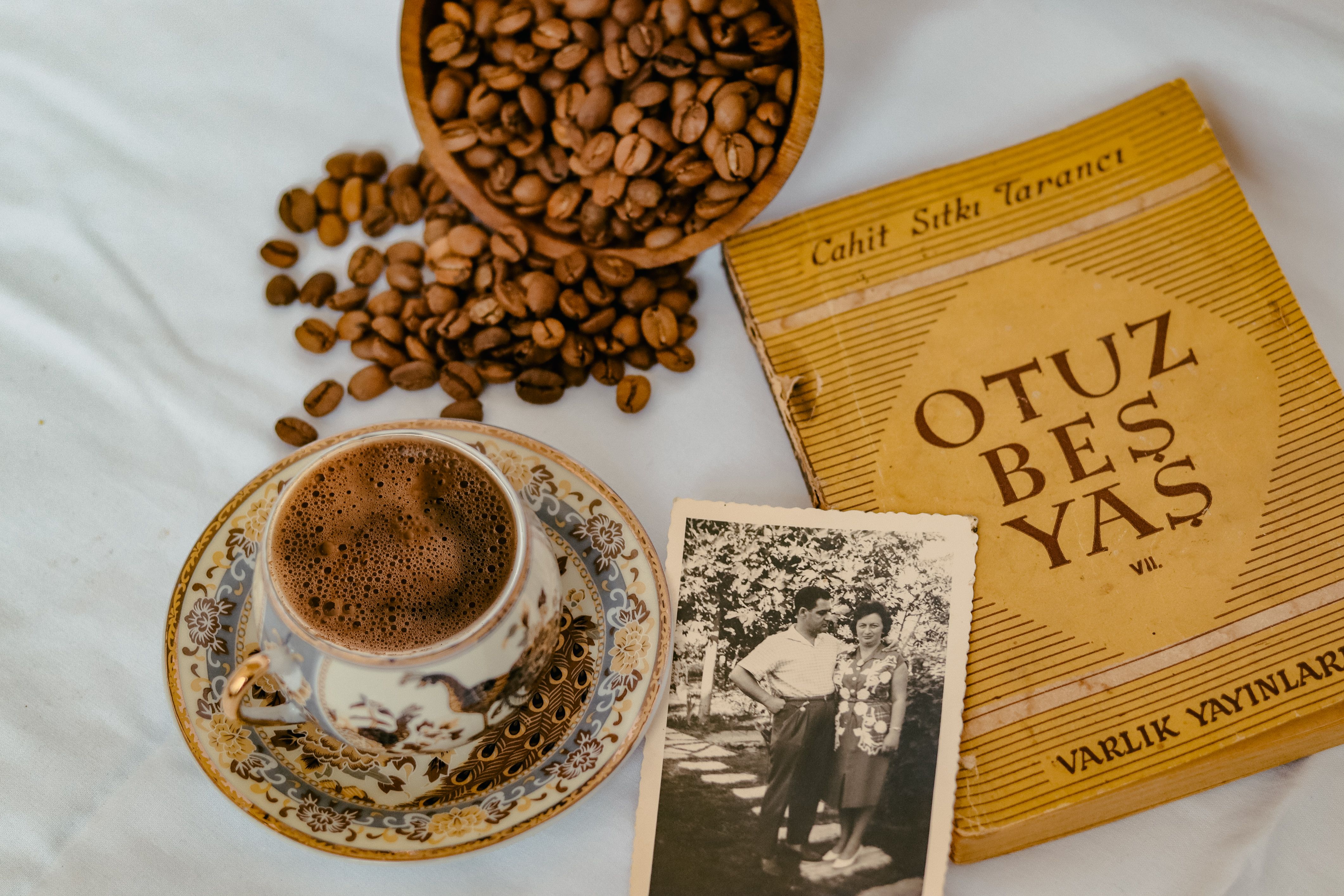 A cup of coffee with coffee beans, an old book, and vintage photo on a white cloth.