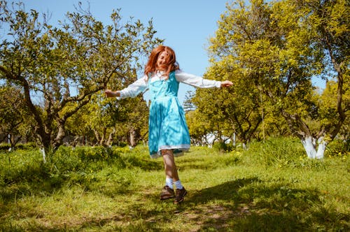 Free Girl in Blue Dress Standing on Green Grass Field Stock Photo