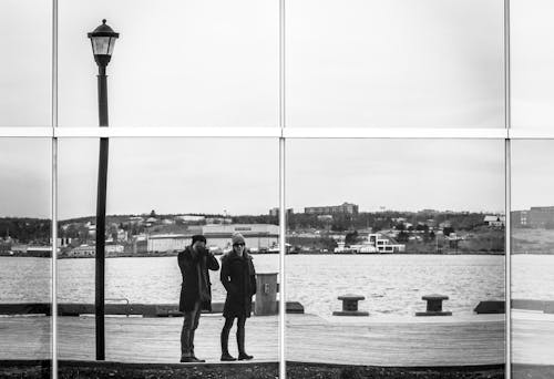 Man and Woman Standing on Concrete Dock in Grayscale Photography