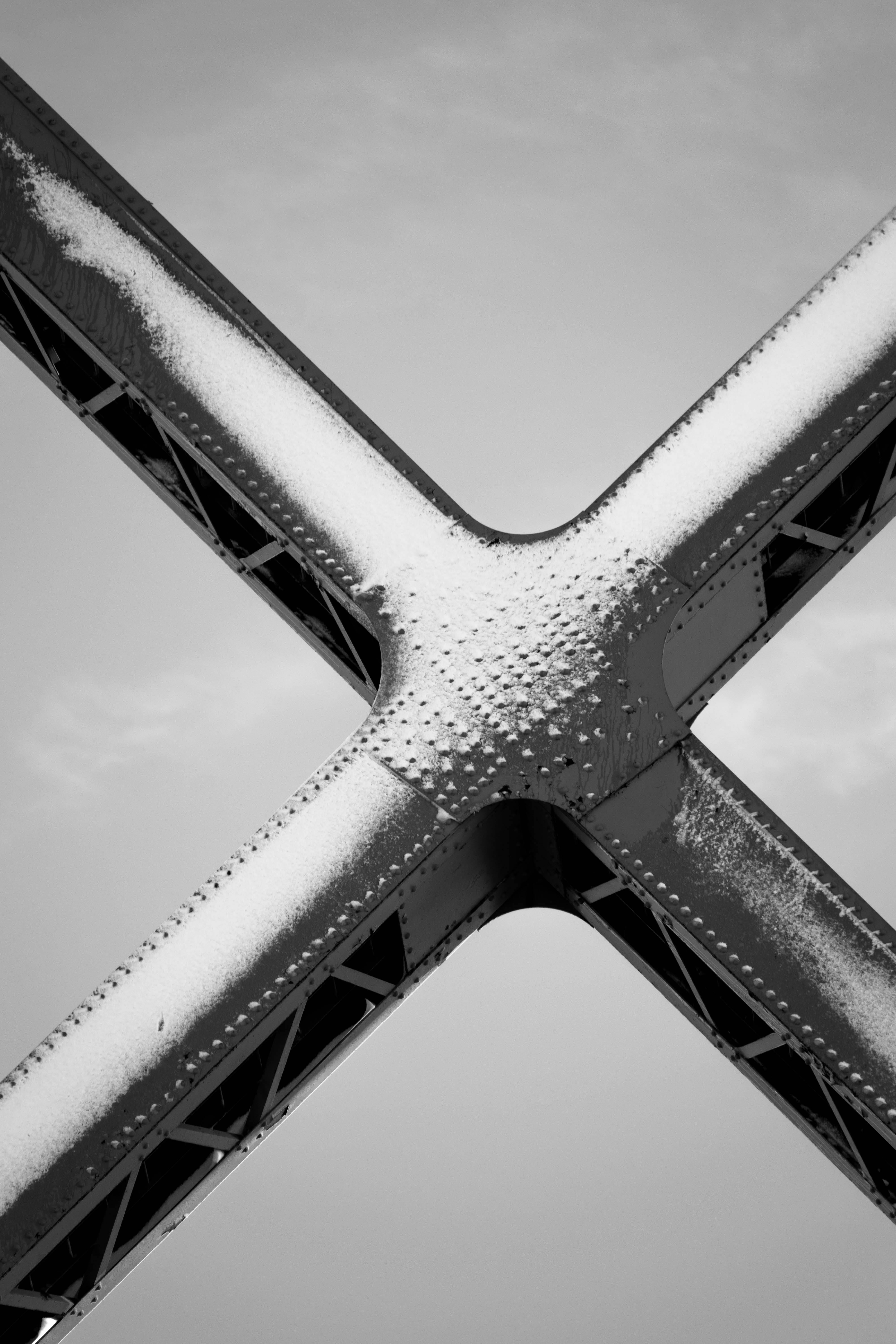 Black and white close-up of riveted steel beams with snow dusting.