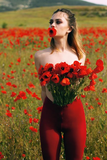 Fotomural Una mujer desnuda sosteniendo un ramo de amapolas en un prado vibrante, exudando belleza y naturaleza.