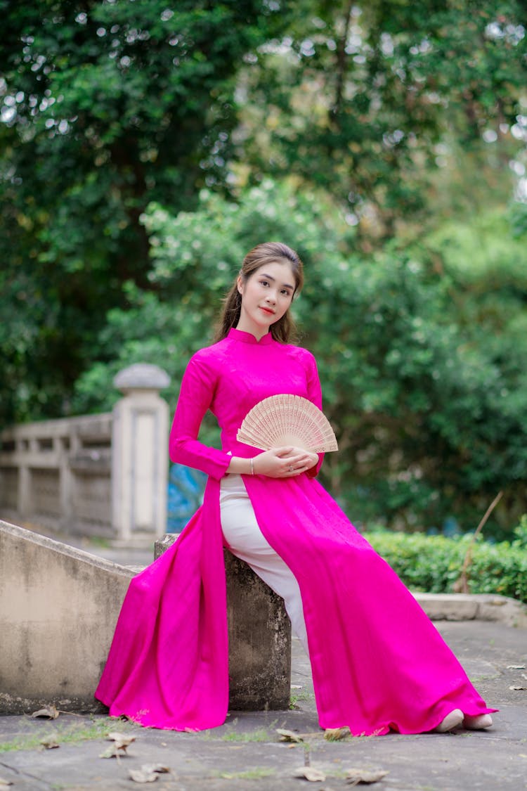 A Woman In A Pink Ao Dai Holding A Fan