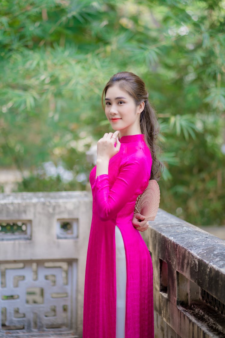 A Woman In A Pink Ao Dai Holding A Fan Behind Her Back