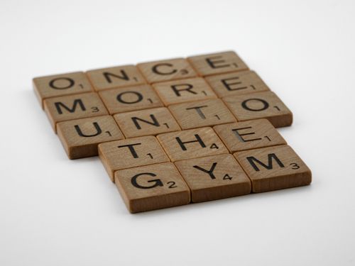 Free Scrabble tiles forming the motivational phrase 'Once More Unto the Gym' on a white background. Stock Photo