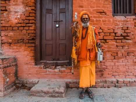 Elderly man in traditional attire posing against a brick wall outdoors.
