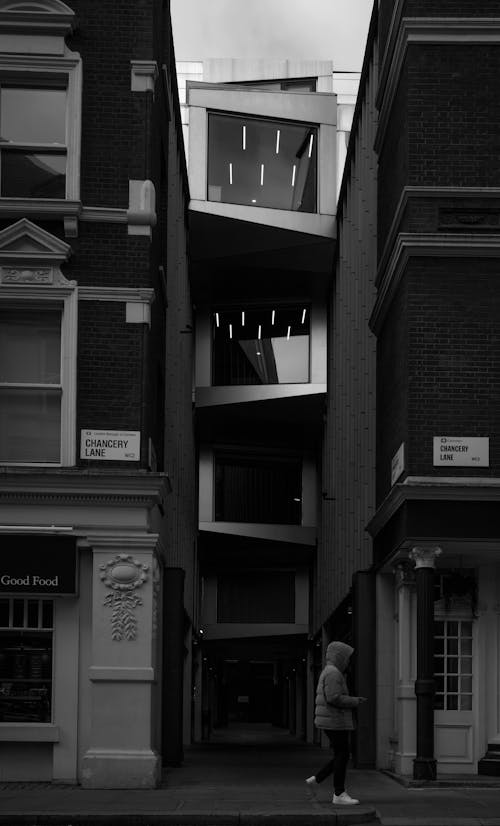 Grayscale Photo of a Person Standing Between Concrete Buildings