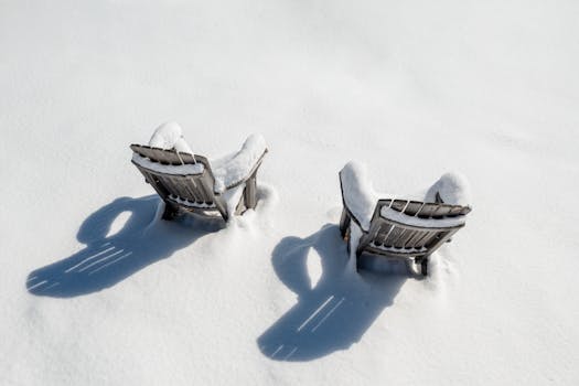 Two wooden chairs covered in snow creating a serene winter landscape scene.