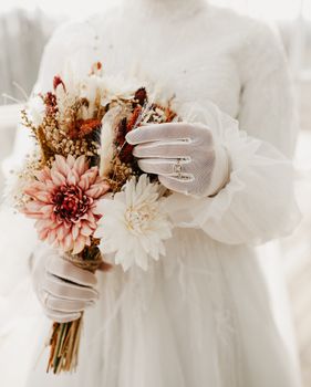 A bride elegantly displays her bouquet while wearing a detailed white wedding dress.