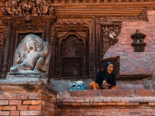 Free A senior woman sits near an ornate temple sculpture in a historical setting, adding a sense of timelessness. Stock Photo