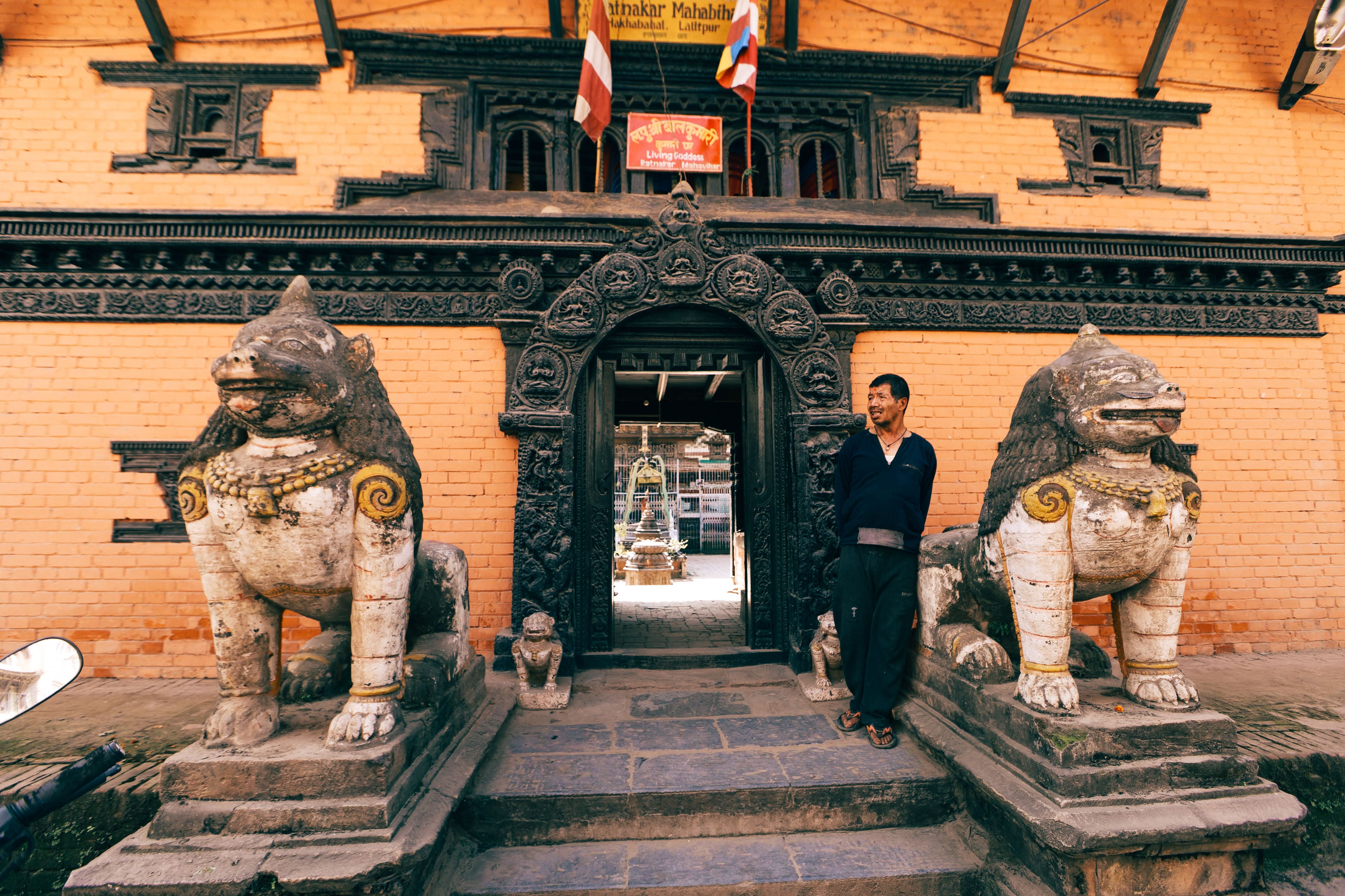 A man stands by a traditional temple entrance in Nepal, flanked by guardian statues.