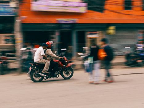 Blurred motion photo of a motorcycle with riders in an urban street setting, showcasing speed and movement.