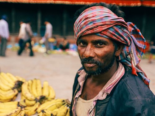 Free Close-up portrait of a bearded man with a headscarf at a market, surrounded by bananas, capturing vibrant street life. Stock Photo