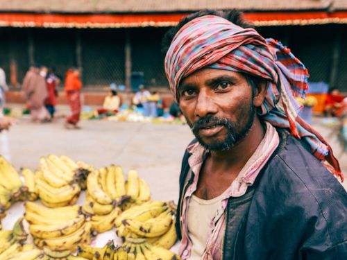 Free Bearded banana vendor in an outdoor market, surrounded by fresh produce. Stock Photo
