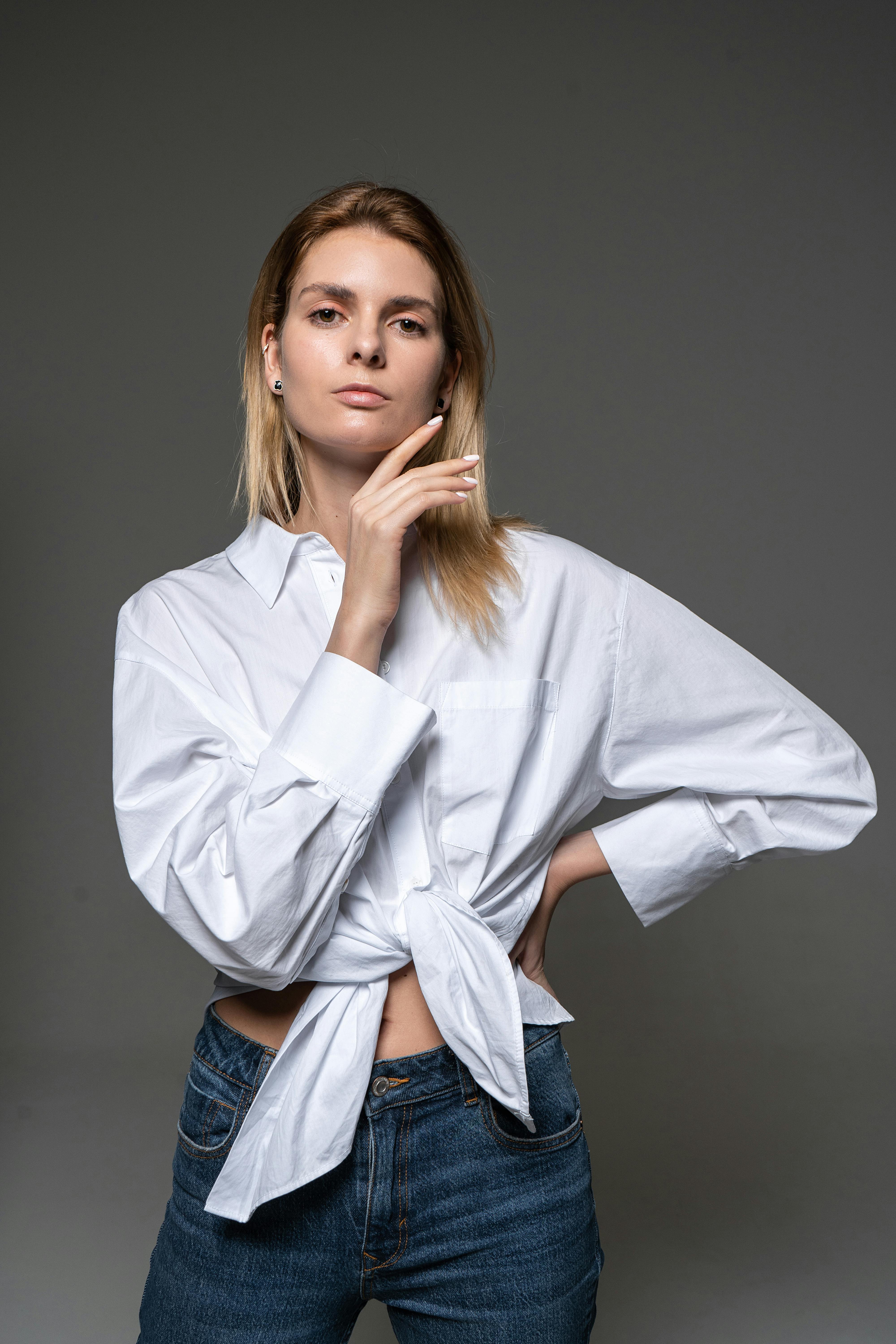 Stylish caucasian woman posing confidently in a studio wearing a casual white shirt and jeans.