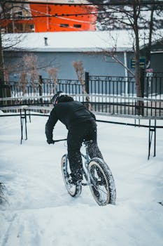 Cyclist riding a bike through snow-covered urban street, showcasing winter sports and adventure.