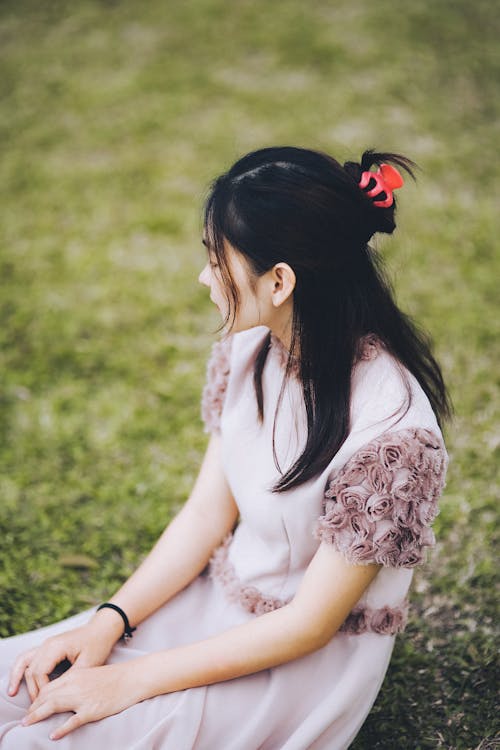 A Woman in Pink Dress Sitting on Green Grass Field