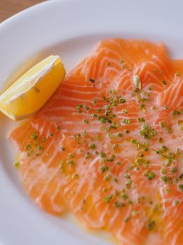 Close-up of fresh salmon carpaccio with a lemon wedge and herbs on a plate.