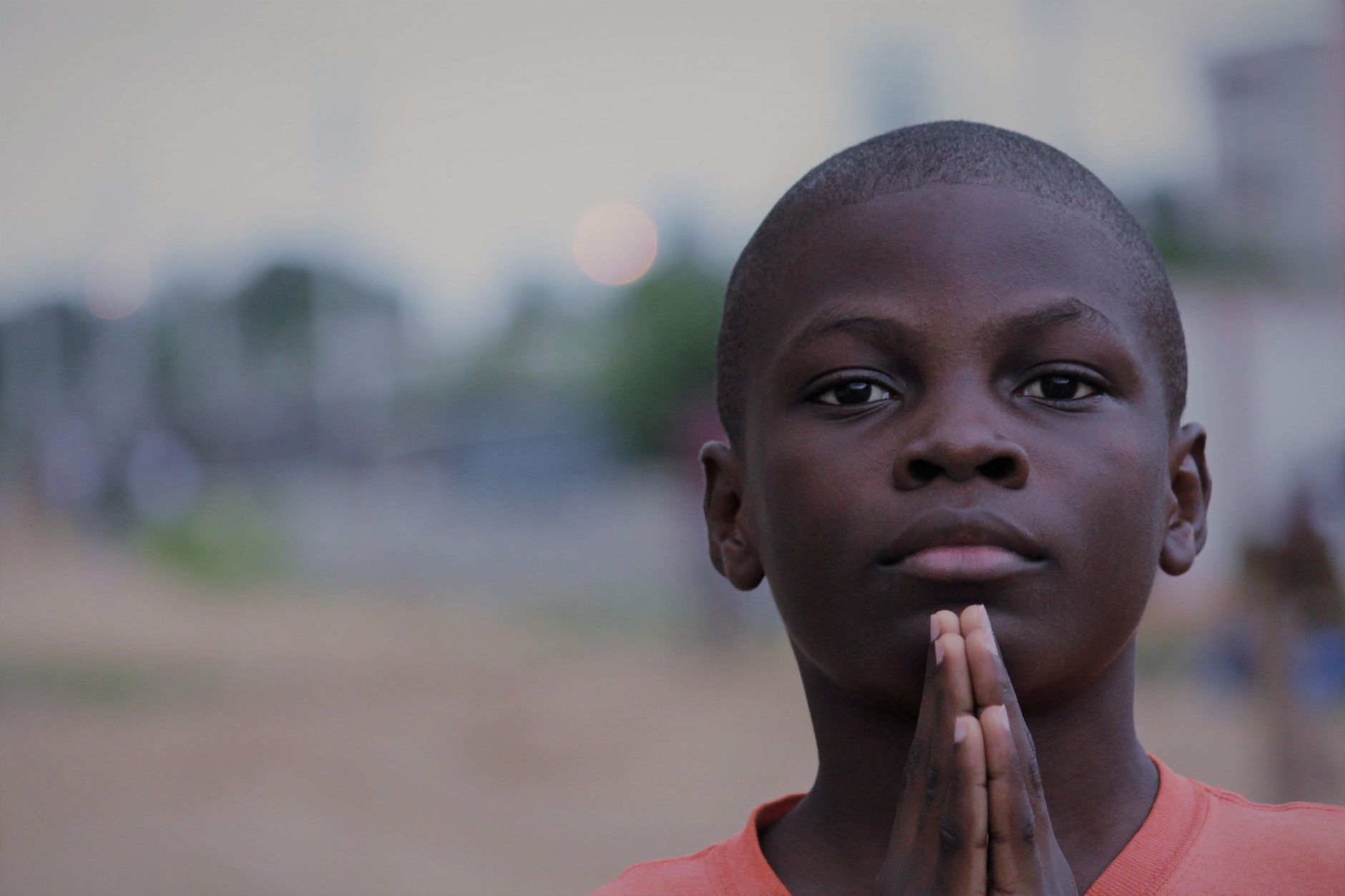 Close-up portrait of a child praying outdoors in Côte d'Ivoire, with a blurred background.