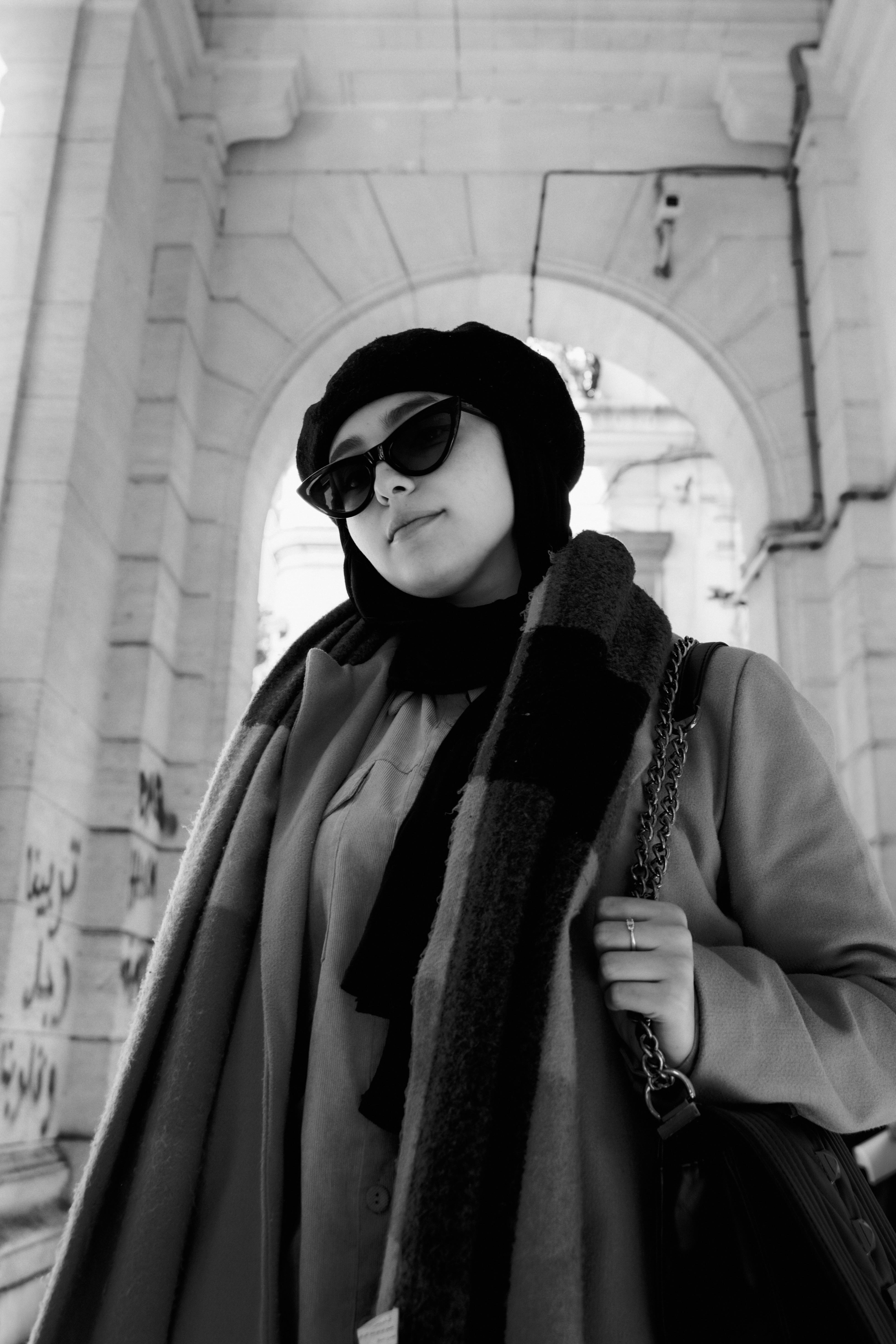 Stylish woman with sunglasses and headscarf under an archway in monochrome.