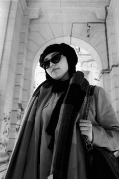 Stylish woman with sunglasses and headscarf under an archway in monochrome.