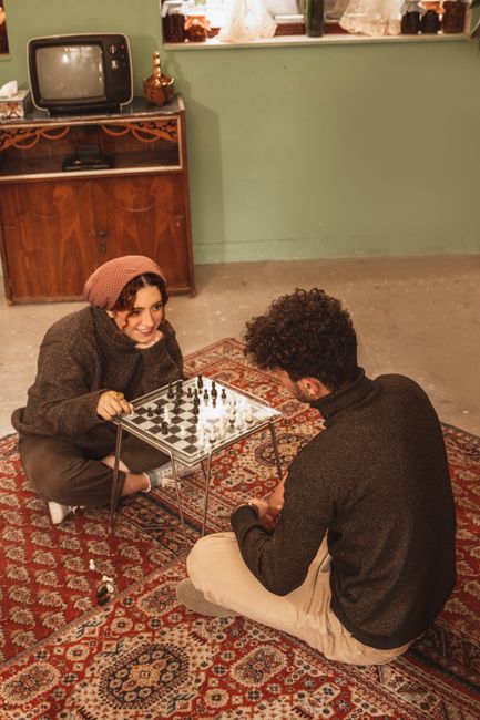 Two people playing chess on a vintage carpet in a cozy indoor setting, both smiling and engaged.