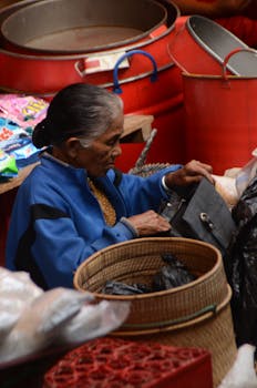 Senior woman in blue jacket shopping at Sulawesi market, Indonesia, examining merchandise.