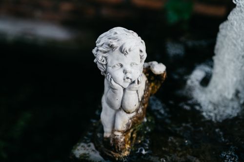 Free A close-up of a cherub statue in a garden fountain, with water flowing around it. Stock Photo