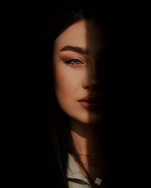 Free Striking half-face portrait of a woman with dramatic lighting and shadow contrast. Stock Photo