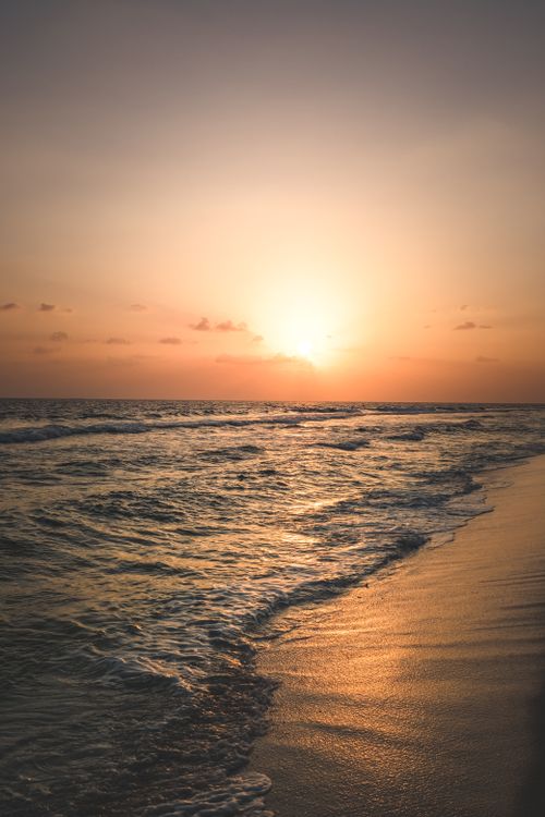 Free Tranquil sunrise over a calm beach with gentle waves lapping the shore. Stock Photo