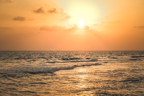 Free Peaceful sunset over gentle ocean waves with an orange sky casting a warm glow. Stock Photo
