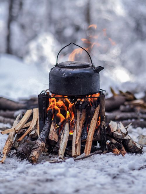 Free Cozy winter camping with a kettle boiling over a rustic campfire amidst snowy surroundings. Stock Photo