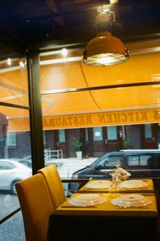Warm restaurant interior featuring a set table beside a large window with street view.