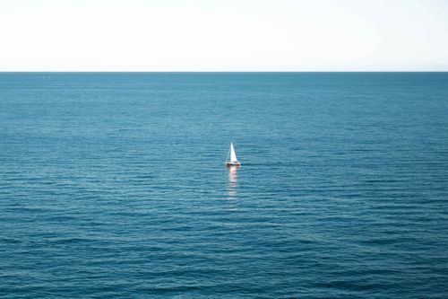 Free A lone sailboat glides across the calm blue ocean under a clear sky, capturing serenity and freedom. Stock Photo