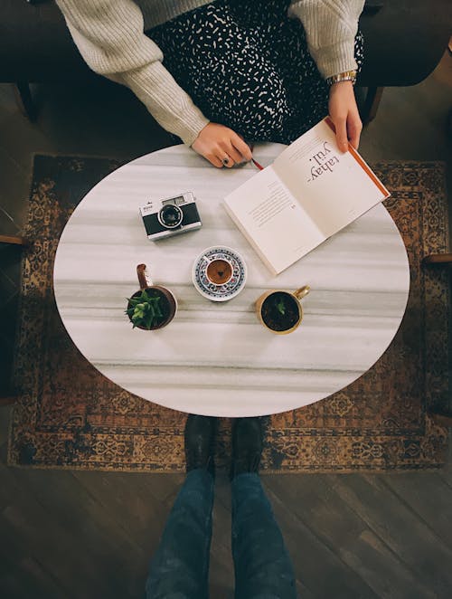 Woman Sitting by Cafe Table with Tea and Open Book