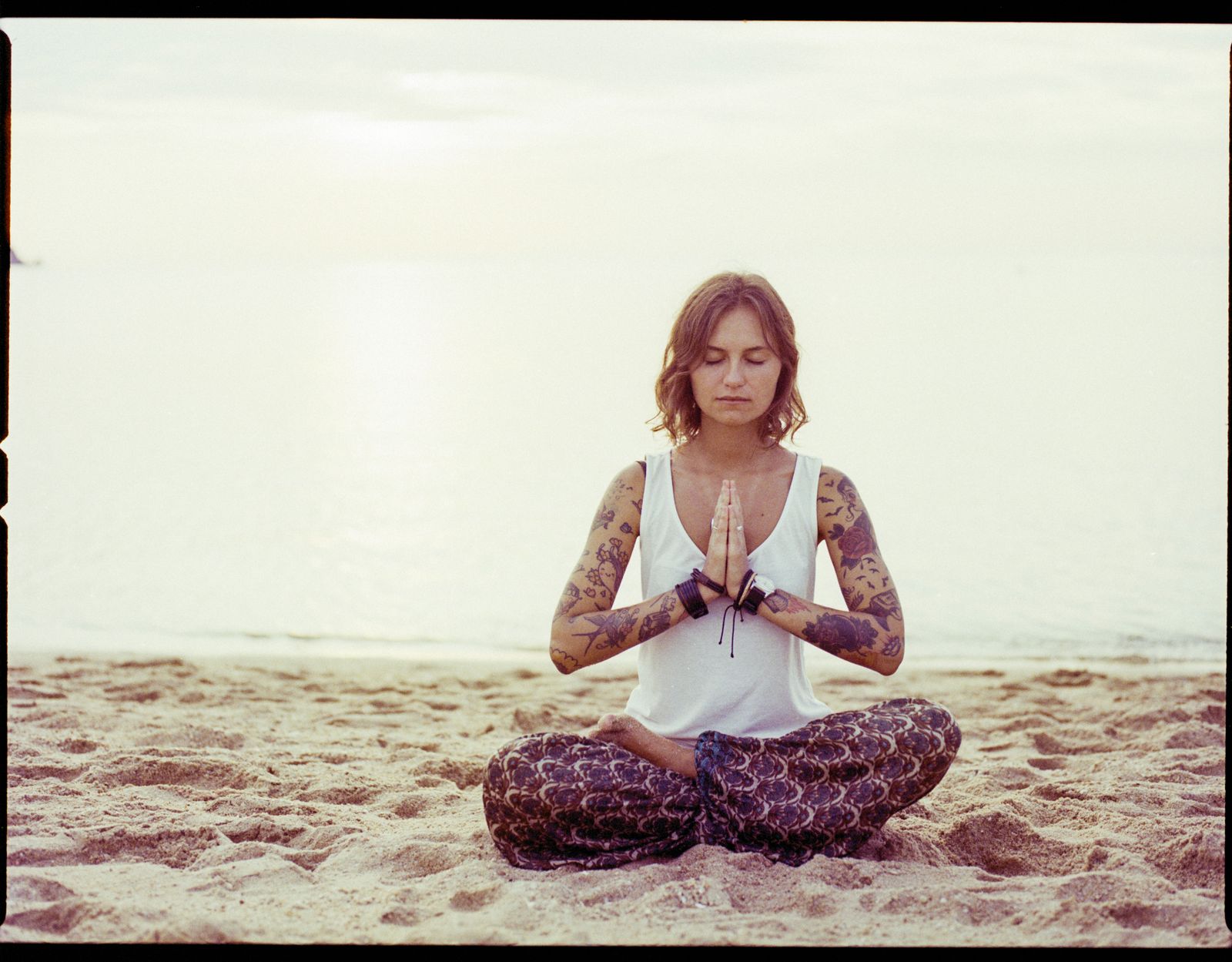 Woman practicing yoga meditation on a tranquil beach at sunrise, embodying surrender and devotion in ishvara pranidhana
