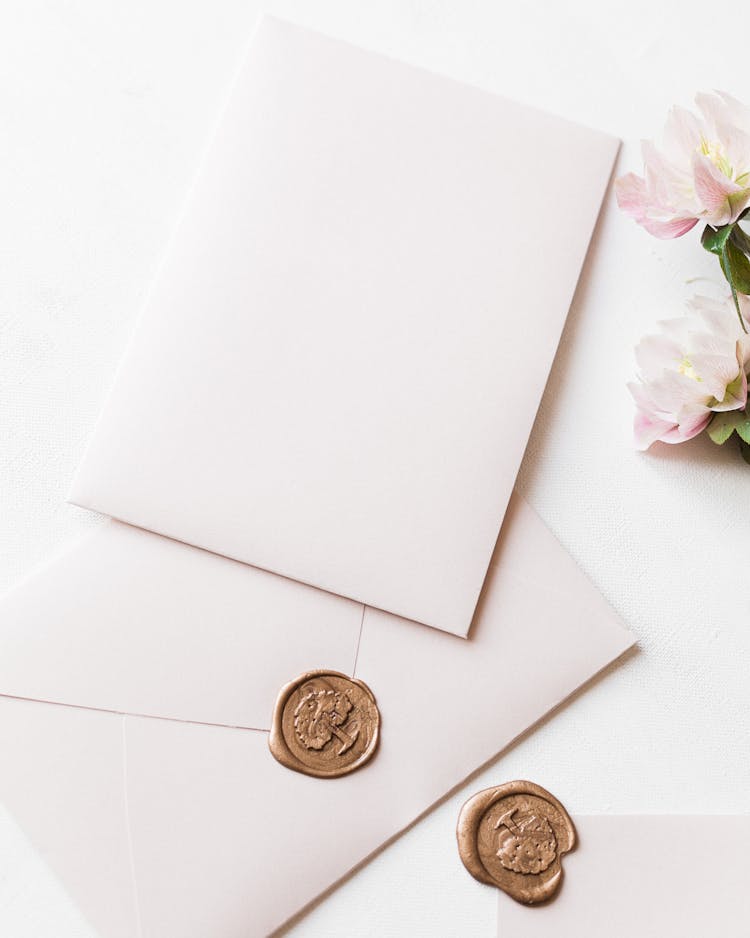 White Envelopes Laying On White Table And Pinkish Flowers