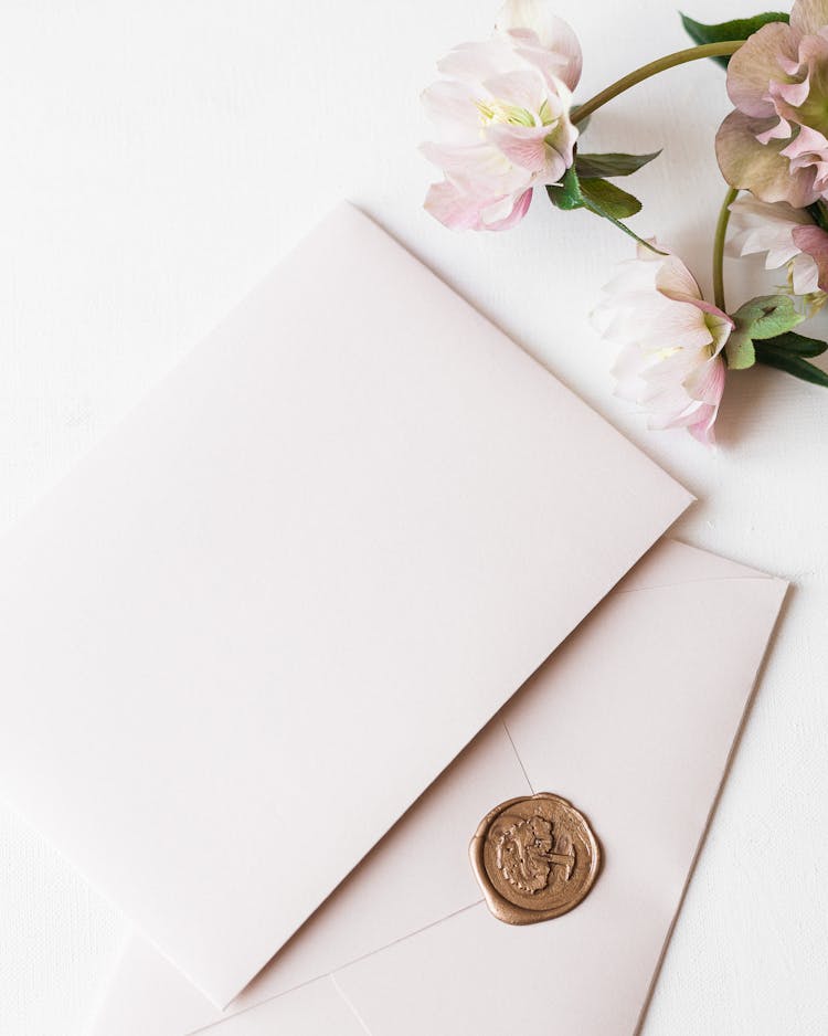 Two White Envelopes And Flowers Laying On White Surface