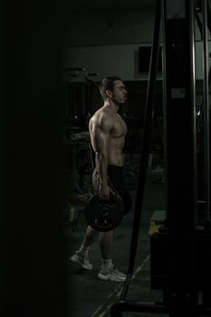 A shirtless man performs weightlifting exercises indoors, showcasing strength and fitness.