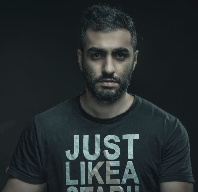 Moody portrait of a bearded man wearing a black t-shirt against a dark background.