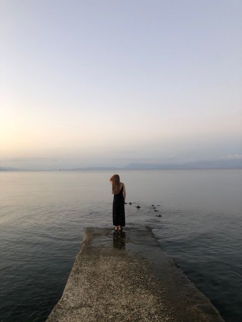 Serene scene of a woman in a black dress standing on a pier in Corfu, Greece.