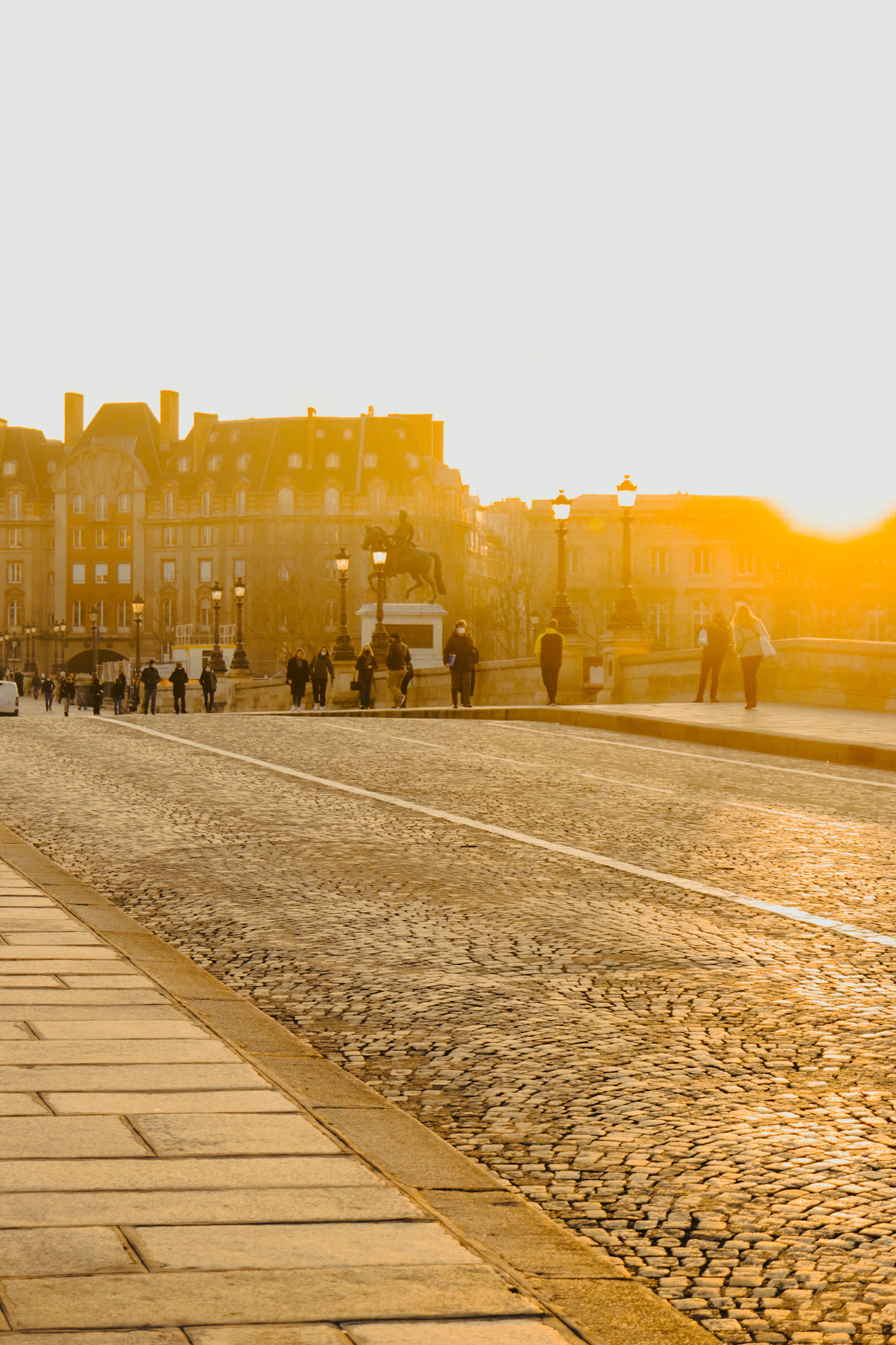 Cobblestone street with people walking towards a glowing sunset, creating a warm urban scene.