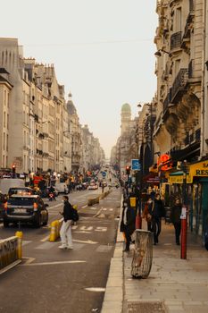 Street scene in Paris with people walking by historic buildings and shops on a busy day.