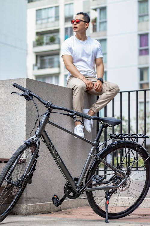 Man Sitting on Concrete Fence Beside a Bike