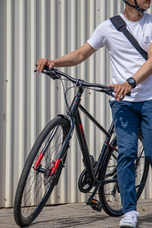 Free Young man in casual attire holding a bike outdoors against a metal panel background. Stock Photo