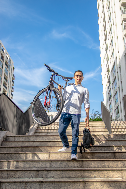 Free Asian man carrying bicycle down stairs in urban setting, Ho Chi Minh City. Stock Photo