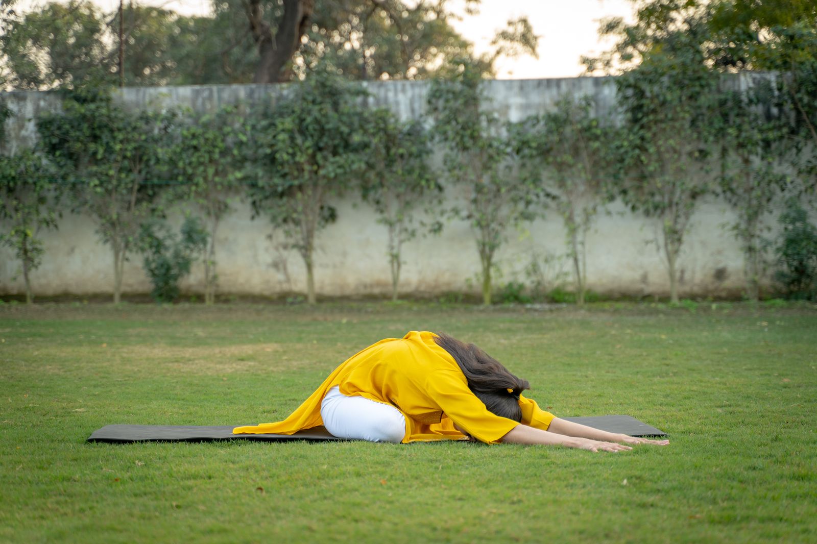 Woman practicing a yoga backbend pose outdoors on a mat surrounded by green grass and trees